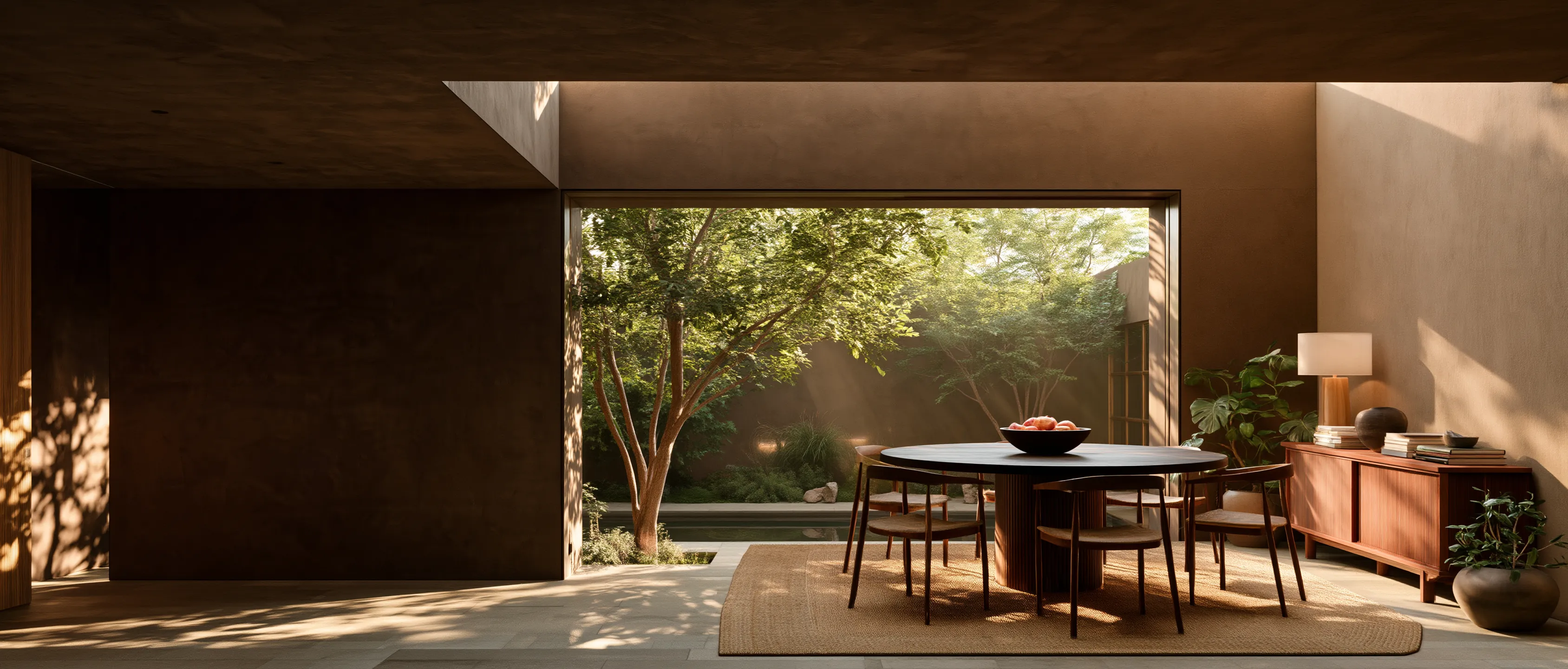 A warm mushroom limewashed dining room with a round table, wooden chairs and a sideboard opening onto a courtyard
